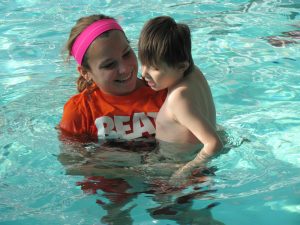 A student helps a child swimming in a pool