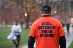 A man in a real veterans wear orange shirt walking on the syracuse quad