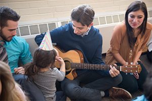 A music education student plays the guitar for a preschool student while others watch