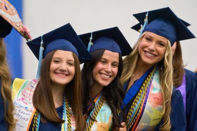three undergraduate students pose in caps and gowns