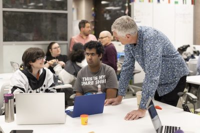 A professor works with students at a table.