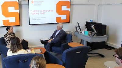 A student speaks with a professor, seated in fron of a large monitor
