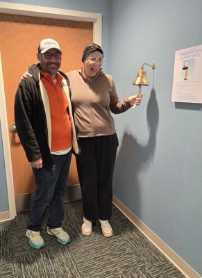 A husband and wife pose together at a chemotherapy center bell