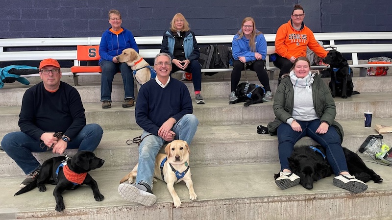 A group of guide dog trainers with their guide dog puppies in the JMA Wireless Dome