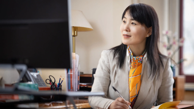 A professor sits at her desk reading a computer screen