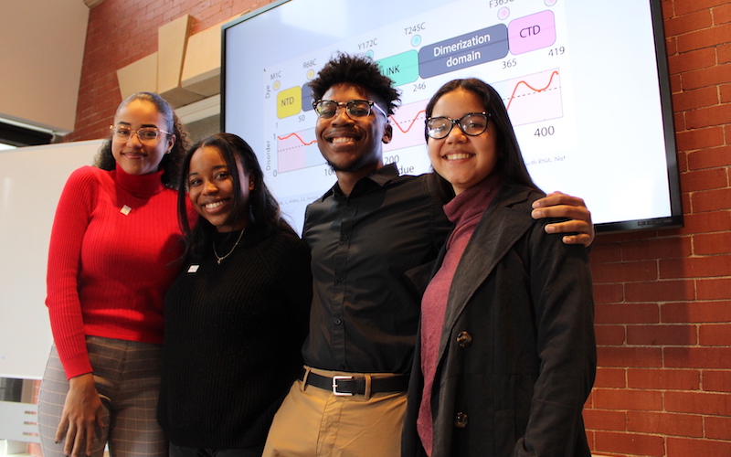 Four LSAMP scholars pose in front of a research slide
