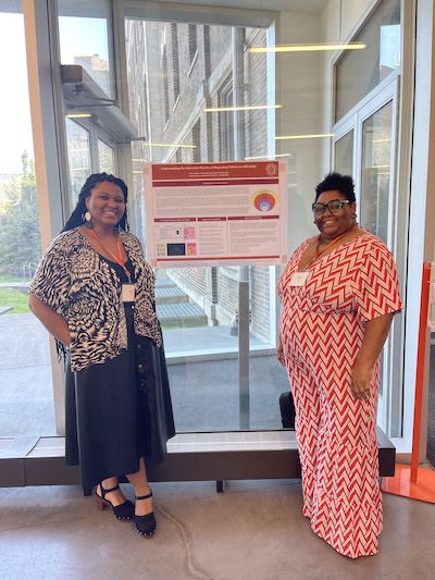 Two black women researchers stand with their poster