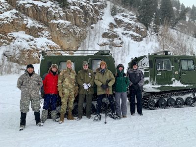 A mix of military and civilians stand in front of a snow vehicle