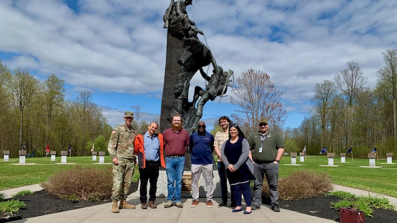 Military and civilians stand in front of a bronze statue