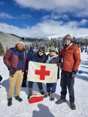 Military and civilians hold a medics flag on a snowy hill.