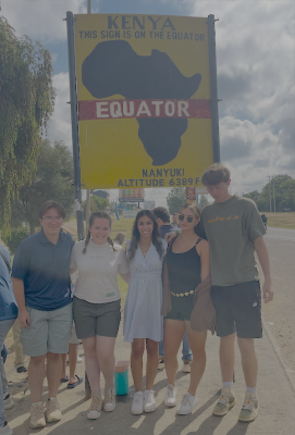 Students stand next to a sign announcing the equator