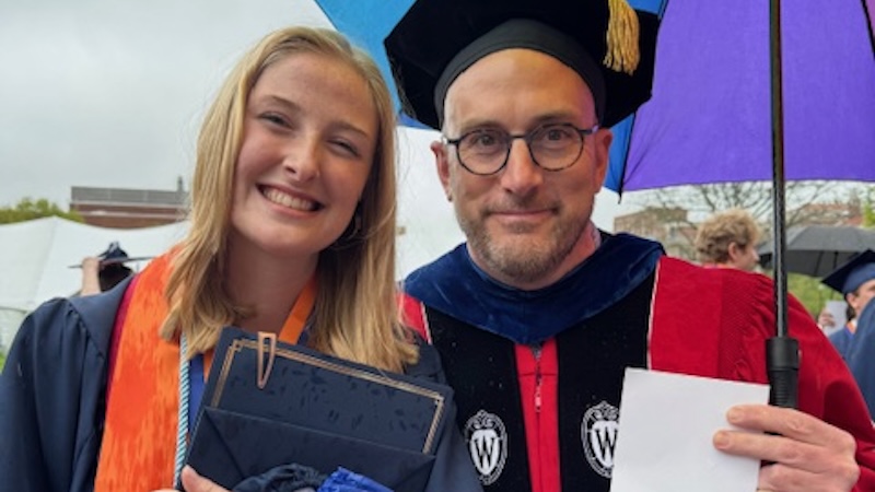 A student and professor in graduation caps and gowns
