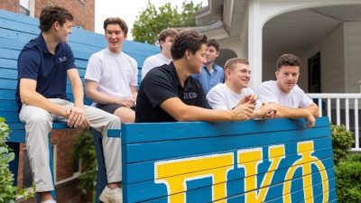 A group of Greek brothers next to their fraternity sign