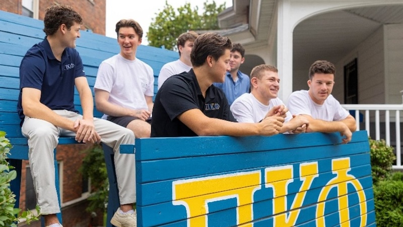 A group of Greek brothers next to their fraternity sign