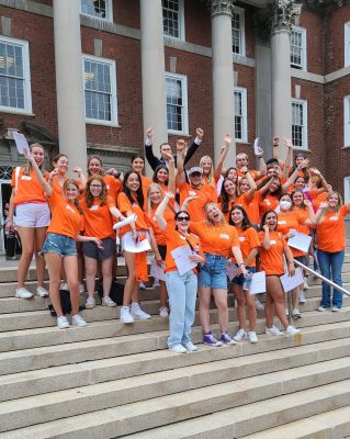 peer advisors in matching orange shirts pose with their hands in the air cheering