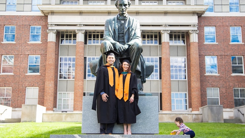 Two graduates stand by a statue