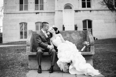 A bride and groom kissing on Syracuse University's "kissing bench"