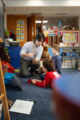 A teacher sits on a carpet with two young students