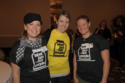 Three women wearing 'label jars not people' t shirts