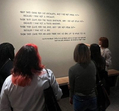 A group of students reads a poem carved into a museum wall