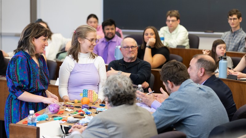 Two women presenting fidget toys to a group of men in a classroom.